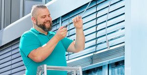 Mann auf einer Leiter mit einem Kabel und einem Steckverbinder in der Hand.